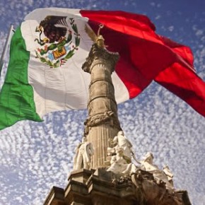 Mexican flag flying behind the Angel of Independence monument in Mexico City.